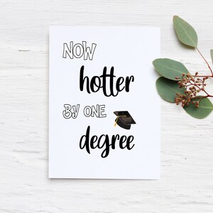 May include: A white graduation card with the text "NOW hotter BY ONE degree" in black script. A small graduation cap illustration is included. The card is decorated with a sprig of greenery.