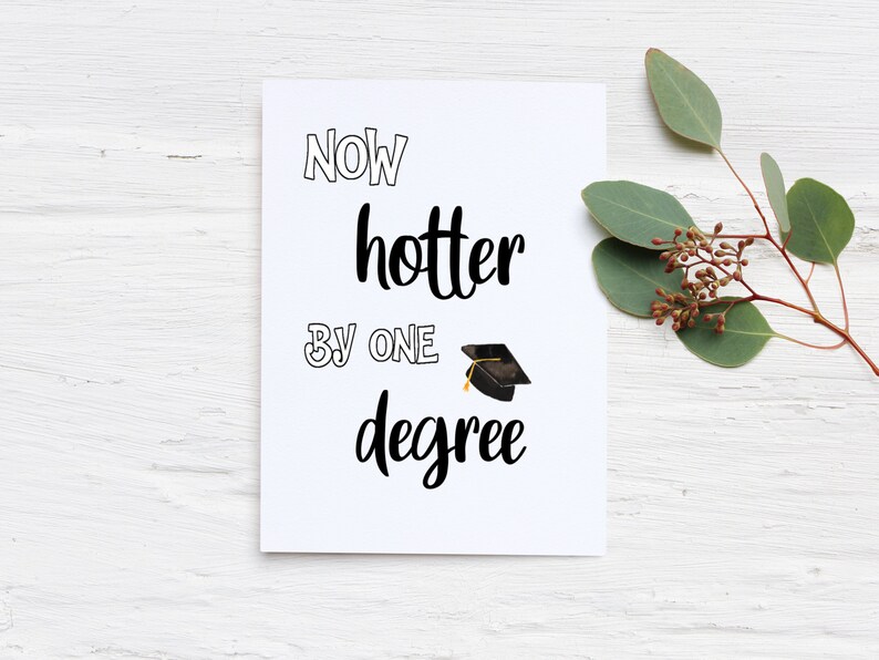 May include: A white graduation card with the text "NOW hotter BY ONE degree" in black script. A small graduation cap illustration is included. The card is decorated with a sprig of greenery.