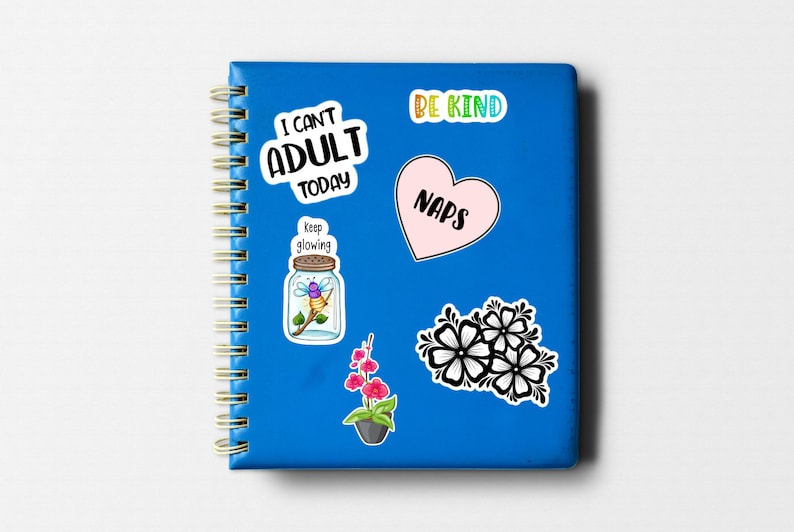 May include: A blue notebook with a spiral binding and several colorful stickers. The stickers feature phrases like "I can't adult today", "Be Kind", "Naps", and "Keep glowing". There is also a sticker of a jar with a firefly inside and a sticker of pink flowers.