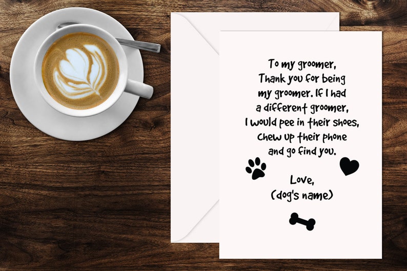 May include: A greeting card with a white envelope, featuring a humorous message for a dog groomer. The card includes text, paw prints, a heart, and a bone graphic. A cup of coffee with latte art sits on a saucer to the left.