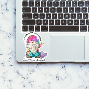 May include: A sticker featuring a cartoon gnome wearing a tie-dye shirt and holding a peace sign. The sticker has the text "I'm mostly peace, love and light and a little go off yourself".