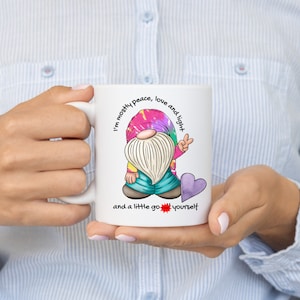May include: White ceramic mug with a colorful tie-dye gnome illustration. The gnome is wearing a blue hat and holding a peace sign. The text on the mug reads "I'm mostly peace, love and light and a little go youself".