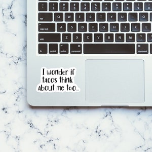 May include: A white laptop computer with a black keyboard and a sticker on the trackpad that says "I wonder if tacos think about me too..."