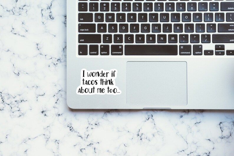 May include: A white laptop computer with a black keyboard and a sticker on the trackpad that says "I wonder if tacos think about me too..."