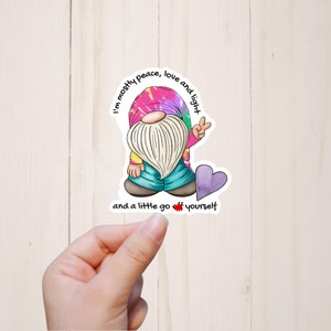 May include: A sticker featuring a cartoon gnome with a tie-dye hat and a peace sign. The gnome is surrounded by the text "I'm mostly peace, love and light and a little go off yourself".