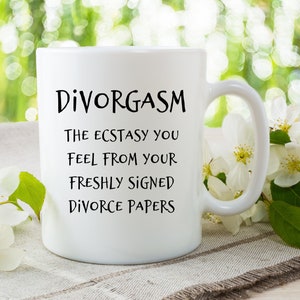 Puede incluir: Taza de caf&eacute; de cer&aacute;mica blanca con texto negro que dice "Divorgasm: The ecstasy you feel from your freshly signed divorce papers". La taza est&aacute; sobre una superficie de lino blanco con flores blancas.