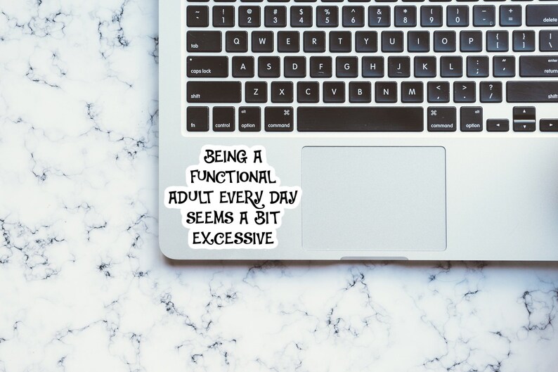 Pu&ograve; includere: Un computer portatile bianco con una tastiera nera e un adesivo sulla parte superiore del touchpad che recita "Being a functional adult every day seems a bit excessive". Il laptop &egrave; su una superficie di marmo bianco.
