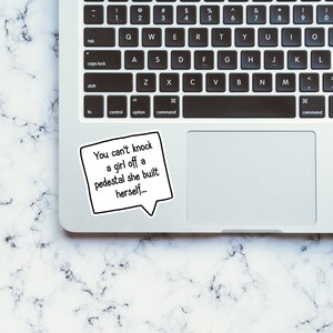 Puede incluir: Un port&aacute;til blanco con un teclado negro y un trackpad negro. Una pegatina con el texto "You can't knock a girl off a pedestal she built herself..." est&aacute; en el port&aacute;til.