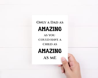 May include: A white greeting card with the text "Only a Dad as AMAZING as you could have a child as AMAZING as me" in black, held by a hand. The card is on a white wooden surface.