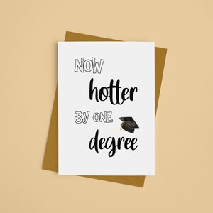 May include: A graduation greeting card with the text "Now hotter by one degree" in black font. A small graduation cap illustration is included. The card is on a brown envelope, set against a beige background.