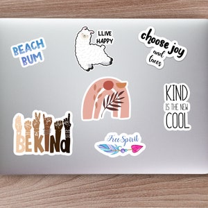 May include: A laptop computer with several stickers on it. The stickers feature various designs and phrases, including a llama, a rainbow, a feather, and the words "Beach Bum", "Live Happy", "Choose Joy and Tacos", "Be Kind", "Kind is the New Cool", and "Free Spirit".