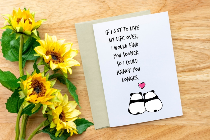 Op de afbeelding: Een wenskaart met de tekst "IF I GOT TO LIVE MY LIFE OVER, I WOULD FIND YOU SOONER SO I COULD ANNOY YOU LONGER" en twee panda-illustraties. De kaart wordt gecombineerd met een beige envelop en zonnebloemen.