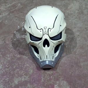 Pode incluir: Um capacete branco em forma de caveira com detalhes pretos e uma prote&ccedil;&atilde;o de queixo cinza. O capacete tem uma malha que cobre as &oacute;rbitas.