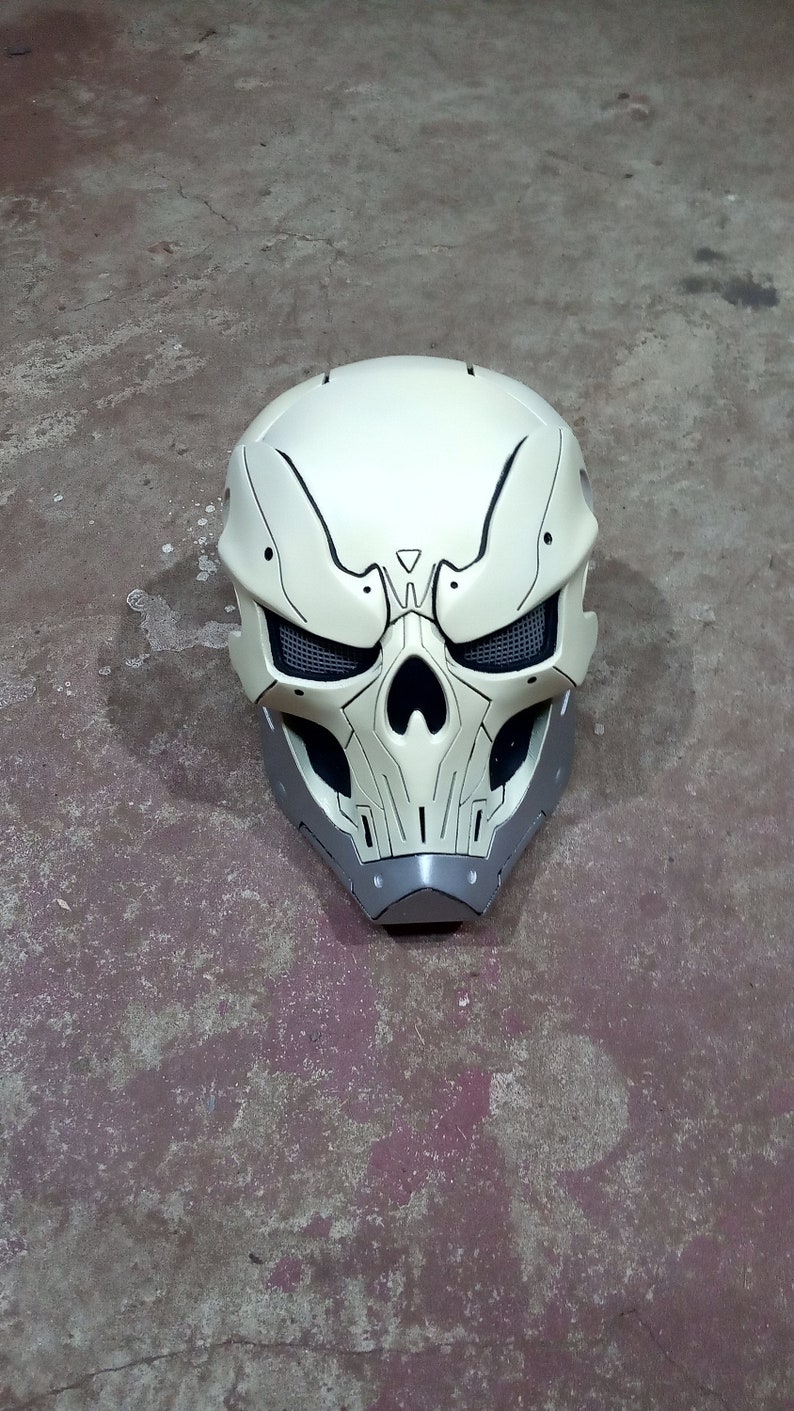 Pode incluir: Um capacete branco em forma de caveira com detalhes pretos e uma prote&ccedil;&atilde;o de queixo cinza. O capacete tem uma malha que cobre as &oacute;rbitas.