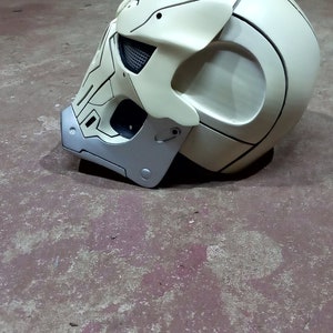 Pode incluir: Um capacete branco com um design de caveira e detalhes pretos. O capacete tem uma viseira prateada e uma correia preta.