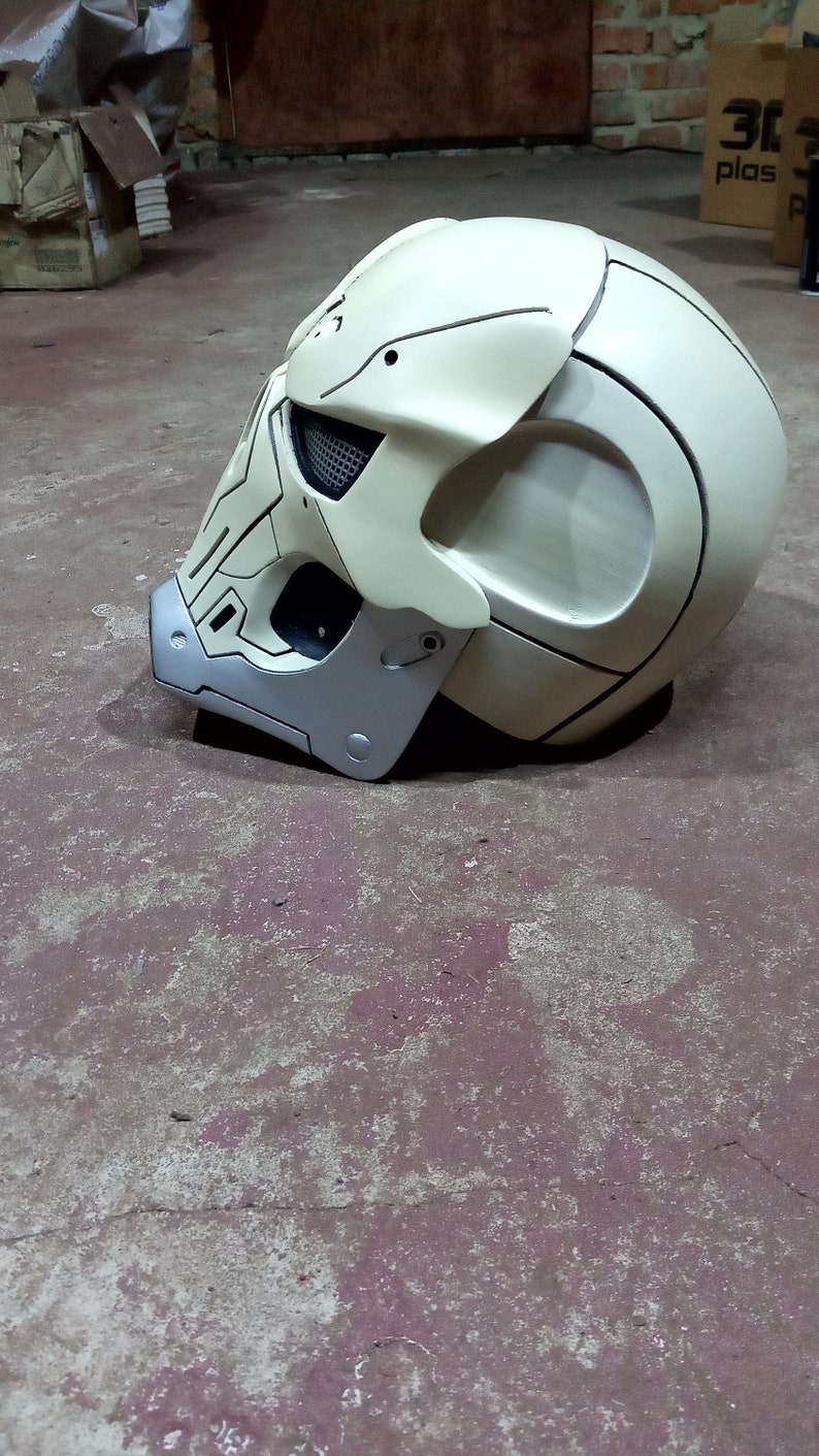 Pode incluir: Um capacete branco com um design de caveira e detalhes pretos. O capacete tem uma viseira prateada e uma correia preta.