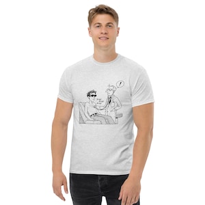 Peut inclure: Un t-shirt gris clair à manches courtes avec un dessin au trait noir et blanc représentant un médecin examinant un patient avec un stéthoscope. Le patient porte des lunettes de soleil et le texte Brap! Brap! Brap! et un point d'exclamation.