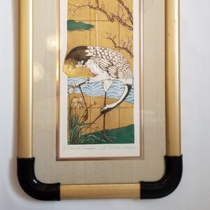 May include: A framed print of a Japanese-style illustration of a crane standing in a garden with a flowering tree and a stream. The print is signed "Crane and Blossoms" by the artist "Seichiro "Mikami" in the lower right corner.