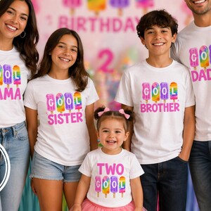 May include: A family wearing matching white t-shirts with colorful popsicle graphics and the words "COOL MAMA", "COOL SISTER", "COOL BROTHER", "TWO COOL", and "COOL DADDY". The background includes a birthday banner.