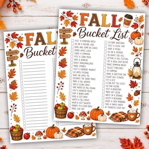 May include: Two printed fall bucket list sheets featuring a checklist of autumn activities. The designs are decorated with colorful fall leaves, pumpkins, a lantern, a basket of apples, and a plaid blanket, all set against a light wood background.