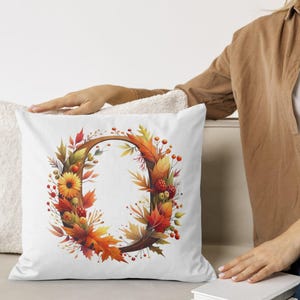 May include: White throw pillow with a fall-themed design featuring a wreath of orange, yellow, and red leaves, berries, and flowers. The wreath surrounds a brown letter "O".