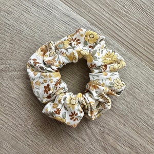 May include: A white scrunchie with a floral pattern in shades of yellow, brown, and green.