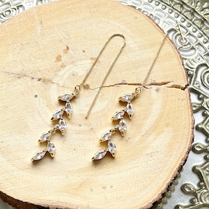 May include: A pair of gold dangle earrings with a delicate leaf design and clear crystal accents.
