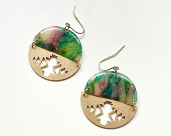 May include: A pair of handcrafted earrings. The top half features a marbled design in shades of green, pink, and purple. The bottom half is a gold-colored metal with a geometric cutout design. Gold-colored ear wires complete the earrings.