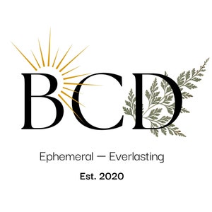 Puede incluir: Un logotipo con las letras "BCD" en una fuente serif, con un diseño de sol sobre la "B" y una ilustración de helecho en la "D". El texto "Ephemeral - Everlasting" y "Est. 2020" están debajo.