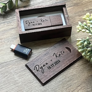 May include: A dark wood rectangular box with a sliding lid and a matching wooden USB flash drive. Both the box lid and the flash drive are engraved with the text Ryan + Kate and the date 10.17.2026. A small black USB-C adapter labeled 10A 240W MAX.