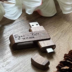 Peut inclure: Clé USB en bois avec connecteur Type-C. La clé est gravée des noms "Ryan + Kate" et de la date "10.17.2026". Le capuchon en bois est détaché et posé à côté de la clé. La clé est en bois brun foncé.