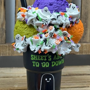 May include: A Halloween-themed sundae in a black cup with a ghost illustration and the text "SHEET'S ABC TO GO DOWN". The sundae features purple, green, and orange scoops, whipped cream, and festive sprinkles.