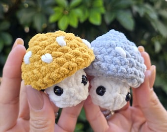 May include: Two crocheted mushroom plushies, one yellow with white dots and one blue with white dots. Both have white fuzzy bodies and black eyes.