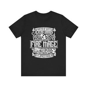 May include: Black t-shirt with a white graphic design. The design includes the words "FIRE MAGE" in a bold font, surrounded by other text and illustrations of flames and mythical creatures. The shirt is made of a soft material.