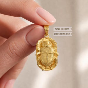 May include: A gold-colored pendant shaped like a scarab beetle with a textured surface and a small bail at the top. The pendant features detailed legs and a rounded body, with the text MADE IN EGYPT and SHIPS FROM USA visible in the background.