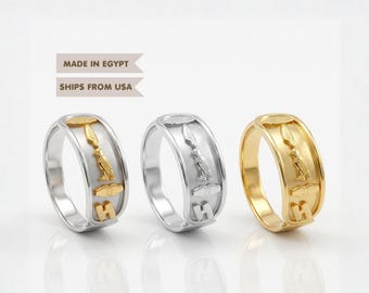 May include: Three rings arranged in a row, featuring embossed Egyptian hieroglyphic symbols including a bird, a feather, and geometric shapes. The first ring is silver-toned, the second is silver-toned, and the third is gold-toned metal.