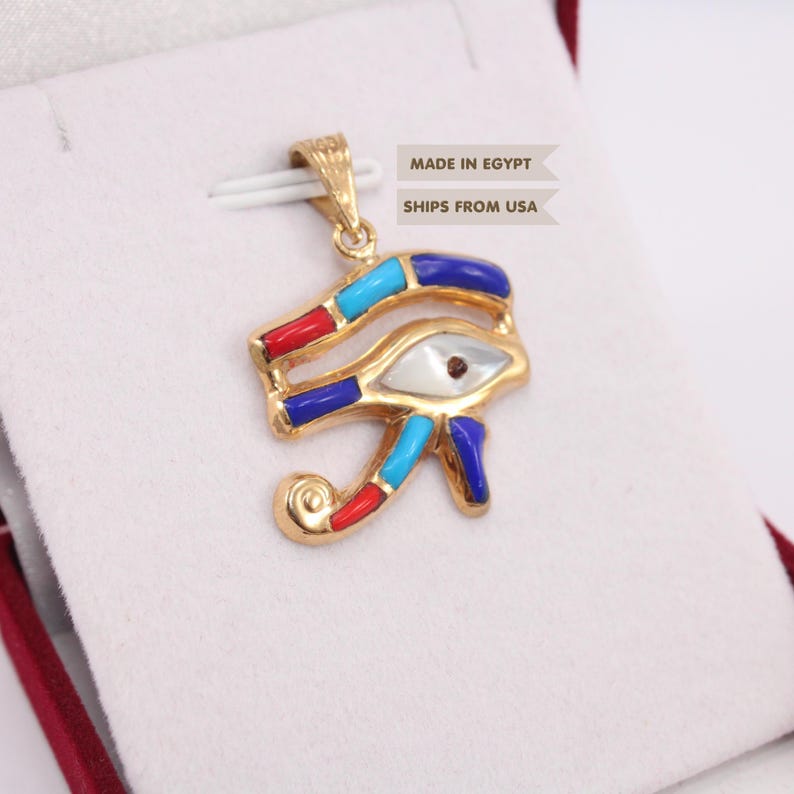May include: A gold-toned Eye of Horus pendant featuring inlaid segments of red, light blue, and dark blue material, with a central white eye element. The pendant includes a bail at the top and displays the text MADE IN EGYPT and SHIPS FROM USA.