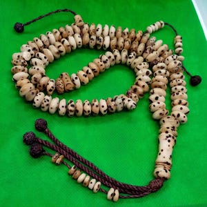 May include: A white and brown prayer beads necklace with brown tassels. The beads are made of natural materials and have a speckled pattern.