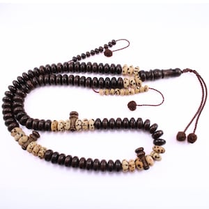 Op de afbeelding: Een donkerbruine houten gebedsketting met afwisselende secties van lichtbeige kralen met donkere vlekken. De ketting heeft een kwast en wordt gepresenteerd op een witte achtergrond.
