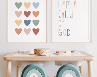 Könnte beinhalten: Zwei gerahmte Drucke an einer weißen Wand. Der Druck links zeigt ein Muster aus 16 bunten Herzen. Der Druck rechts zeigt den Text "I AM A CHILD OF GOD" in bunten Buchstaben.