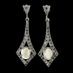 May include: A pair of silver drop earrings featuring a diamond-shaped frame encrusted with small dark gray marcasite stones. Each earring centers an oval-shaped, iridescent white cabochon stone, suspended from a triangular top piece.