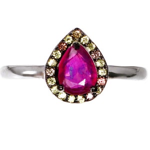 May include: A pear-shaped ruby ring with a halo of smaller colorful gemstones. The ring is set in silver.