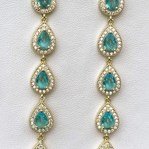 May include: A pair of long, gold drop earrings with five teardrop-shaped blue stones set in a halo of smaller clear stones.