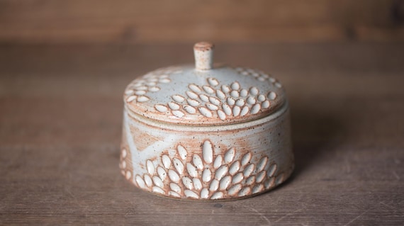 Hand-carved floral relief on a speckled ceramic jar — the carving detail is the kind of quiet flex that separates a real craft artist from a production line.