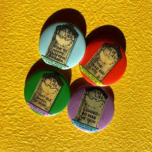 Könnte beinhalten: Vier bunte runde Buttons mit einem Grabstein-Design und dem Text "Here Lies". Jeder Button hat einen anderen Spruch: "Gone to Happy Haunting Grounds", "The Dead End Kid", "That Ole Ghoul or Mine" und "Loaded - So Was The Gun".