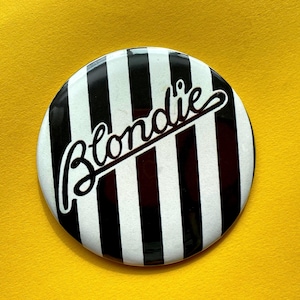 Op de afbeelding: Een zwart-wit gestreepte knop met het woord "Blondie" in cursief.