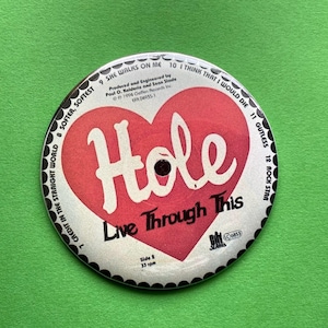 Op de afbeelding: Een witte vinylplaat met een rood hart waarop de band Hole en de albumtitel "Live Through This" te zien zijn. De plaat is omgeven door een zwart-witte rand met de tracktitels die eromheen staan.