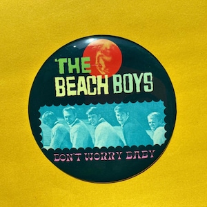 Könnte beinhalten: Ein runder, schwarzer Button mit dem Text "THE BEACH BOYS" in Grün und Weiß und dem Satz "DON'T WORRY BABY" in Rosa. Der Button zeigt eine rote Sonne und ein Foto der Band.
