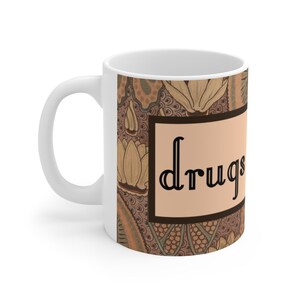 May include: White ceramic mug with a brown and beige floral pattern. The mug has a black rectangular label with the word "drugs" printed in a decorative font.