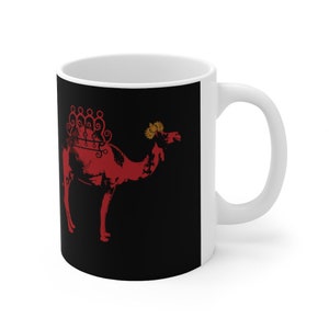 May include: White ceramic mug with a black background and a red camel silhouette. The camel has a decorative design on its back and a gold crown on its head.